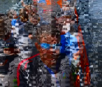 A orange boat with a number of attendees enjoying the sunshine in Odense docks on a boat trip